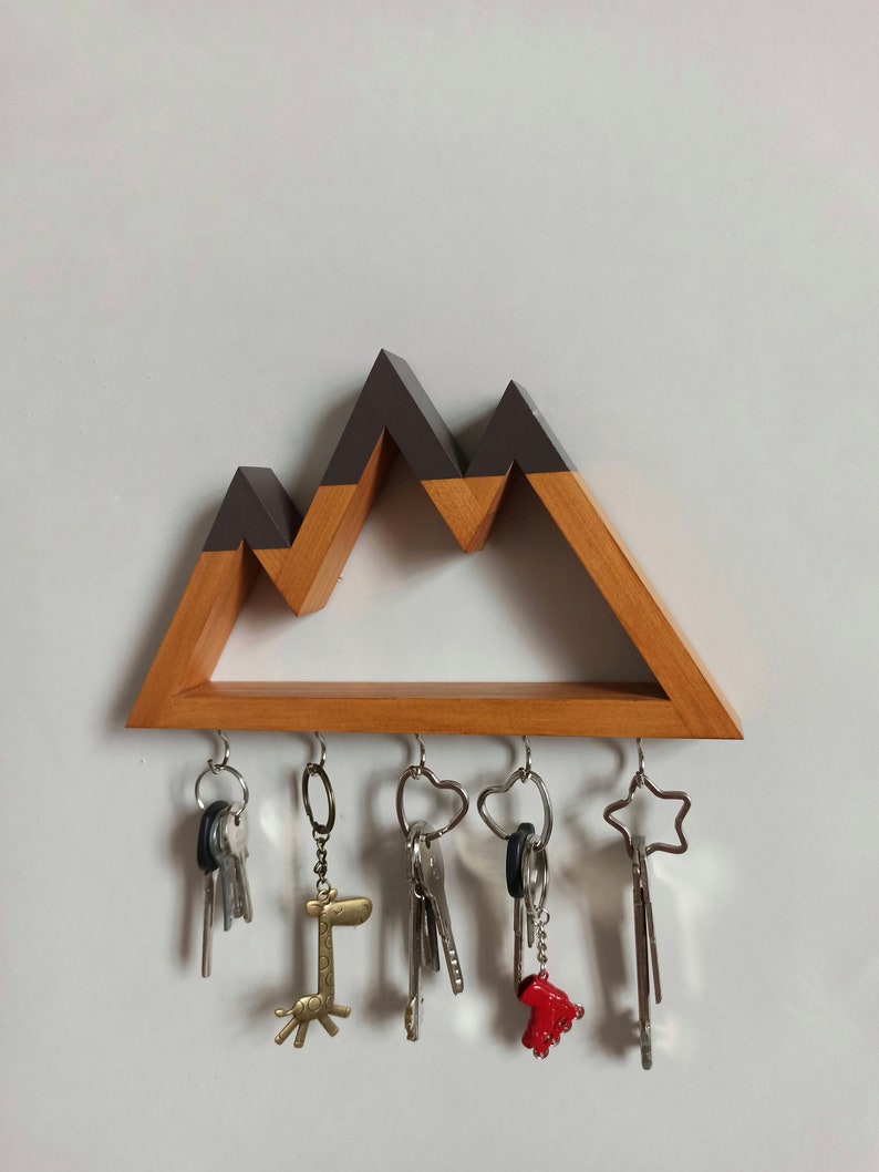 May include: Wooden key holder shaped like a mountain range with a brown wood base and a dark gray top. Five keys are hanging from hooks on the bottom of the holder.
