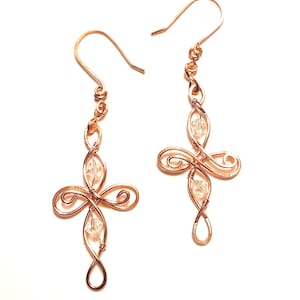 May include: A pair of copper-colored wire-wrapped earrings featuring a cross-shaped design. Each earring includes two clear faceted crystal beads integrated into the wire structure and is finished with a simple curved ear wire hook for hanging.
