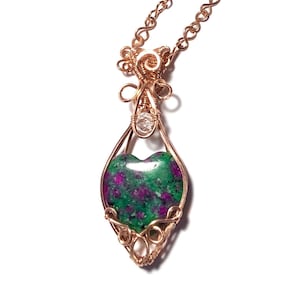 May include: A copper wire pendant necklace with a heart-shaped gemstone. The gemstone has a green and purple pattern. The necklace features a delicate chain and intricate wirework, showcasing a unique, artistic piece of jewellery.