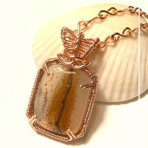May include: A copper wire wrapped pendant featuring a brown and white agate stone with a copper butterfly design.