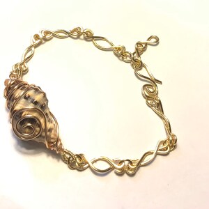 May include: A gold wire wrapped seashell bracelet with a gold chain link clasp.