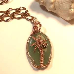 May include: A copper wire wrapped pendant necklace featuring a green oval stone with a copper wire palm tree design.