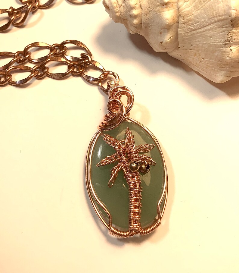 May include: A copper wire wrapped pendant necklace featuring a green oval stone with a copper wire palm tree design.