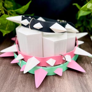 Puede incluir: Tres collares coloridos para mascotas con púas blancas y rosas. El collar superior es negro con tachuelas blancas en forma de diamante. El collar del medio es rosa con púas blancas y rosas. El collar inferior es verde menta con púas rosas.
