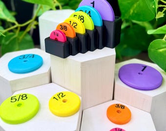 May include: A set of circular plastic measuring discs in various colors including purple, blue, lime green, yellow, orange, and pink. Each disc is marked with a black fraction or whole number: 1/4, 3/8, 1/2, 5/8, 3/4, and 1. A black holder stores the discs.
