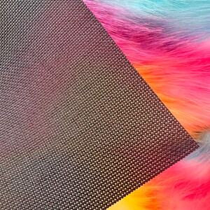 May include: A close-up of a rainbow-colored faux fur fabric with a dark brown, textured backing. The fur transitions from yellow to orange, pink, blue, and green. The backing has a woven pattern.