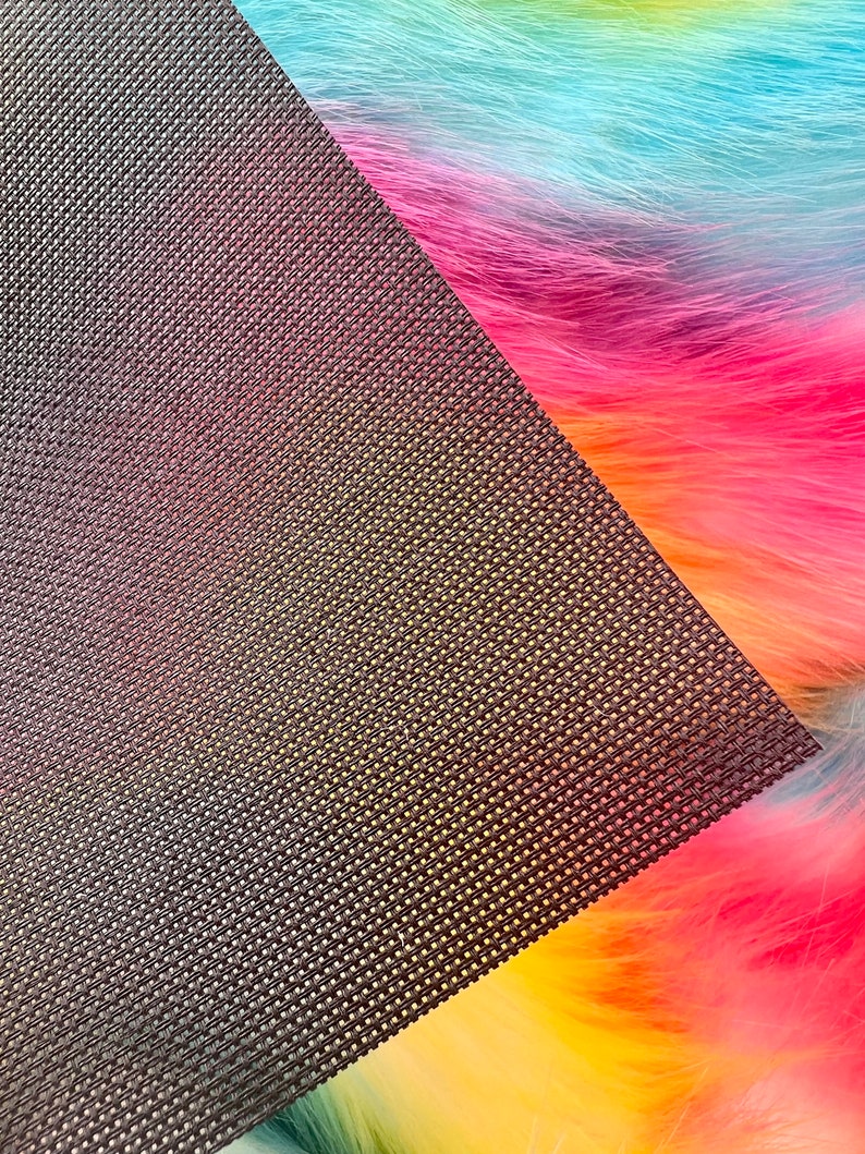 May include: A close-up of a rainbow-colored faux fur fabric with a dark brown, textured backing. The fur transitions from yellow to orange, pink, blue, and green. The backing has a woven pattern.