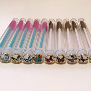 Può includere: Dieci tubi di plastica trasparente con tappi bianchi e disegni di farfalle. Ogni tubo contiene un piccolo pennello rosa, blu o bianco.
