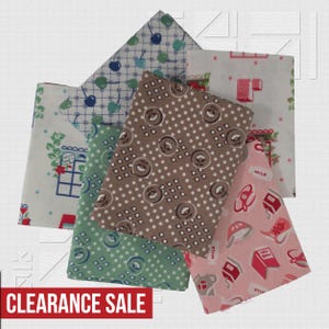 May include: A collection of five folded fabric swatches featuring various patterns including blue cherries on a grid, brown polka dots with floral motifs, green polka dots, and pink kitchen-themed prints with milk cartons and cookbooks.