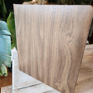 May include: A wooden panel with a natural wood grain pattern. The panel is a light brown color with darker brown streaks and knots, giving it a rustic appearance. The panel is angled, showing its side profile.
