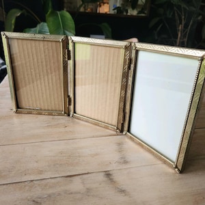 May include: A triptych photo frame featuring three connected rectangular panels with a metallic gold finish. Each frame has a textured, beaded border and is hinged together, allowing the unit to stand independently on a flat surface.
