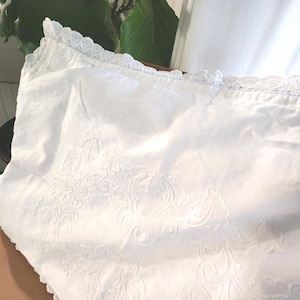 May include: A white pillowcase with an embossed floral design and a delicate lace trim along the edge. The pillowcase is made of a soft, possibly cotton, fabric. The design is visible across the surface.