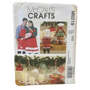 May include: McCall's Crafts sewing pattern M6219. The pattern features images of Christmas-themed aprons and stuffed figures, including a Santa Claus and gingerbread man. The cover has a white background with red and green accents.