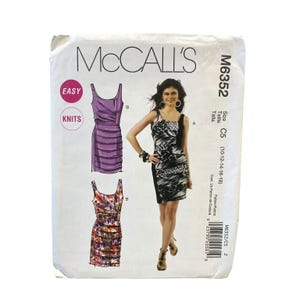 Puede incluir: Patrón de costura McCall's M6352 para vestidos. La imagen muestra ilustraciones de tres diseños de vestidos, incluyendo un vestido fruncido morado y un vestido con estampado en blanco y negro. El patrón está etiquetado como "Easy Knits".