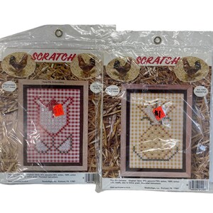 Puede incluir: Dos paquetes de kits de bordado Teneriffe con un diseño de cuadros rojos y blancos con una flor blanca y un diseño de cuadros amarillos y blancos con una piña. Los paquetes están etiquetados como "Scratch Teneriffe Embroidery" e incluyen el número de artículo y el nombre del diseño.