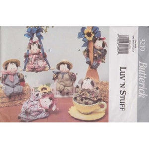 May include: A sewing pattern for five different stuffed animal dolls. The dolls are dressed in various outfits, including a gingham dress, a plaid shirt, and a floral dress. The pattern is titled "Luv 'N Stuff" and is from Butterick.