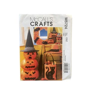 May include: McCall's Crafts M5724 sewing pattern envelope featuring Halloween-themed projects. The cover displays a stack of three fabric pumpkins wearing a polka-dot witch hat, a wreath with bat decorations, and a black tote bag with a cat silhouette.