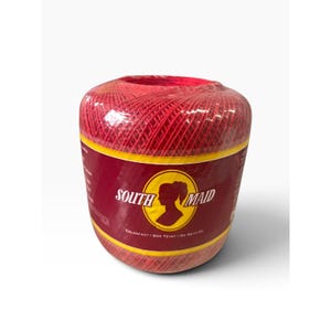 May include: A cylindrical ball of bright red crochet thread wrapped in clear plastic. A maroon label features the text SOUTH MAID in white, a yellow circular emblem with a silhouette of a person, and the words COLORFAST, BON TEINT, NO DESTINE.