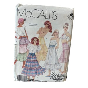 Puede incluir: Patrón de costura McCall's para una falda de capas. El patrón incluye cinco estilos de faldas diferentes, cada uno con un diseño y una longitud diferentes. El patrón es para tallas de señorita 30. El texto en el patrón dice "Focus on Overlock (Serger) Sewing."