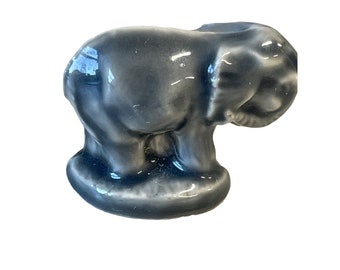 Può includere: Una piccola statuetta di elefante in ceramica grigia. L'elefante è in piedi su una base e ha la proboscide arrotolata.