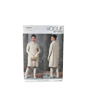 May include: A Vogue Patterns sewing pattern envelope V1911 for a knee-length, light beige coat with a high collar and three-quarter sleeves. The front shows two views of the coat worn with matching gloves and boots against a gray backdrop.