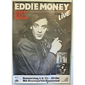May include: Black and white concert poster for Eddie Money's "Ticket to Rock Paradise" live show. The poster features a portrait of Eddie Money holding a cigarette. The text includes the date and venue.