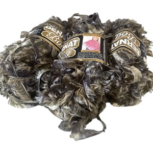 May include: Three skeins of Bernat yarn in shades of brown, gray, and white. The yarn has a fringed texture, and each skein has a label with the brand name and a picture of a knitted garment. The yarn is suitable for knitting and crochet projects.