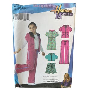 Puede incluir: Patrón de costura Simplicity Hannah Montana para niñas, tallas 8-16. El patrón presenta a una niña con un chándal rosa e ilustraciones de varias prendas, incluyendo un vestido, una blusa, una falda y un pantalón.