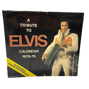 May include: A vintage 1978-79 Elvis Presley calendar. The cover is black with the text "A Tribute to Elvis" in orange and white. An image of Elvis in a white jumpsuit with red and gold accents is featured. The calendar is an authorized collector's edition.