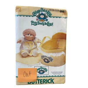 May include: A vintage Cabbage Patch Kids sewing pattern with a yellow and white gingham pattern. The pattern is for a doll carrier and includes a doll in a yellow and white dress. The pattern number is 6661.