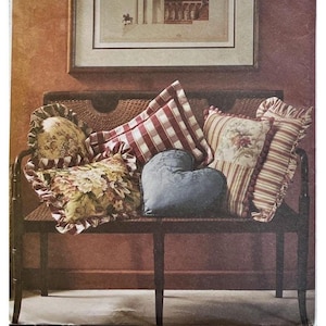 May include: A dark wooden bench featuring a collection of decorative pillows, including a heart-shaped blue pillow, a red and white checkered pillow, a floral print pillow with ruffled edges, and a striped pillow with a floral center panel.