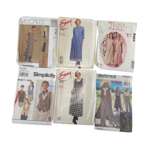 Puede incluir: Seis paquetes de patrones de costura vintage. Los paquetes presentan imágenes de vestidos, chalecos y pantalones. Las marcas incluyen McCall's, Simplicity y Butterick. Los paquetes están en fundas de plástico y tienen texto como "Easy to Sew" y "Glamour".