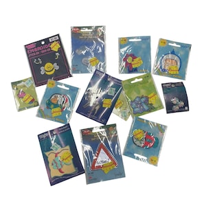 May include: A collection of embroidered patches in various shapes and designs, including a bee, flowers, and a road sign. The patches are packaged on colorful cards with the text "EMBROID STICK-ON/IRON-ON".