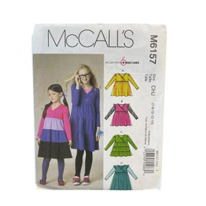 May include: A McCall's M6157 sewing pattern envelope for a long-sleeve dress with a wrap-style bodice and tiered skirt. The front shows two children wearing different versions of the dress, alongside illustrations of six variations labeled A through F.