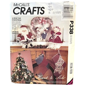 Puede incluir: Un patrón de manualidades vintage de McCall's Crafts para hacer decoraciones navideñas. El patrón incluye instrucciones para hacer una corona en forma de corazón, una media, un árbol de Navidad y una muñeca de Papá Noel. El patrón se titula "A Mop Top Christmas" y "Un Noel Original".