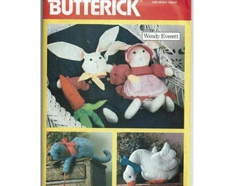 May include: A Butterick pattern envelope featuring soft toy patterns. The top section shows a bunny with a carrot and a bunny wearing a bonnet. The bottom section shows a blue cat and a white goose. The text "Butterick" is at the top.