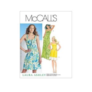 Könnte beinhalten: Nähmuster von McCall's für ein Kleid von Laura Ashley. Das Muster zeigt drei verschiedene Kleidstyles, eines in Grün, eines in Gelb und eines in Blau und Weiß.