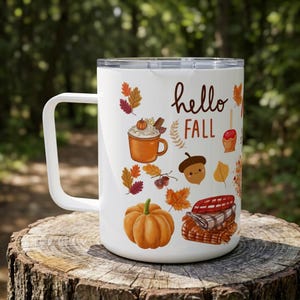 May include: A white travel mug with a clear lid and a handle, featuring a colorful autumn-themed graphic print. The design includes the text "hello FALL" surrounded by illustrations of a pumpkin, an acorn, a mug of cocoa, and fall leaves.