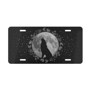 May include: A black and white image of a wolf howling at the moon. The moon is full and surrounded by a wreath of flowers. The background is a dark blue with white stars.