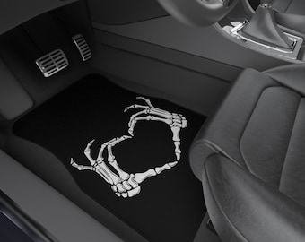 May include: Black car floor mat with a white skeleton hand design making a heart shape.