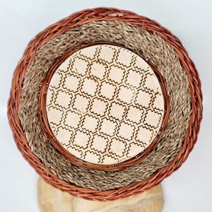 May include: A woven basket with a round, light brown base and a woven lid with a geometric pattern. The lid is made of natural materials and has a light brown color.