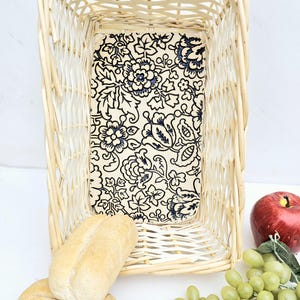 May include: A wicker basket with a floral patterned liner. The basket is filled with two loaves of bread, a bunch of green grapes, and a red apple.
