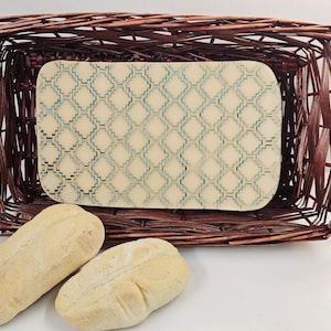 May include: A rectangular woven basket with a patterned serving tray inside, and two loaves of bread in front. The tray has a cream background with a teal geometric design. The basket is brown.