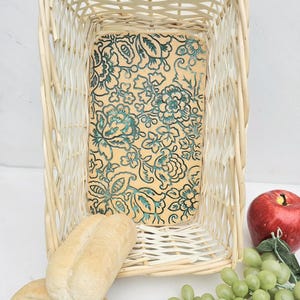 May include: Rectangular wicker basket with a floral patterned interior. The basket contains two bread rolls, a red apple, and a bunch of green grapes. The basket is empty.