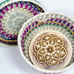 May include: A woven basket with a colorful striped pattern and a lid. The inside of the basket has a ceramic base with a decorative design.