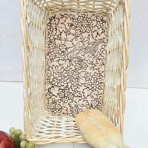 May include: A white wicker bread basket with a floral patterned liner. Two rolls of bread are in the basket.