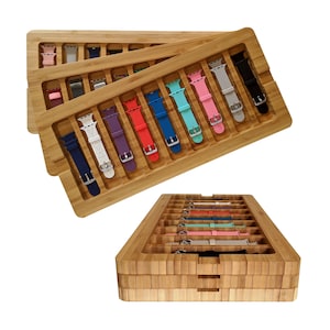 May include: A wooden storage box with multiple compartments for holding watch bands. The box is made of light brown bamboo and has a stacked design. The compartments are filled with colorful silicone watch bands.