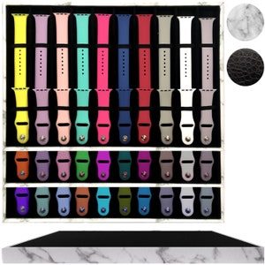 May include: A white organizer with a black base and marble-like design, holding 30 colorful silicone watch bands in a grid pattern.