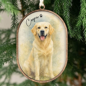 May include: Oval wooden ornament featuring a watercolor painting of a golden Labrador Retriever. The dog is smiling with its tongue out. The name "Cooper" is written above the dog, with a paw print symbol.