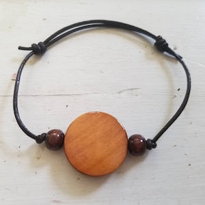 May include: A wooden bracelet with a large, round, light brown wooden bead and two smaller, dark brown wooden beads. The bracelet is made of black cord.